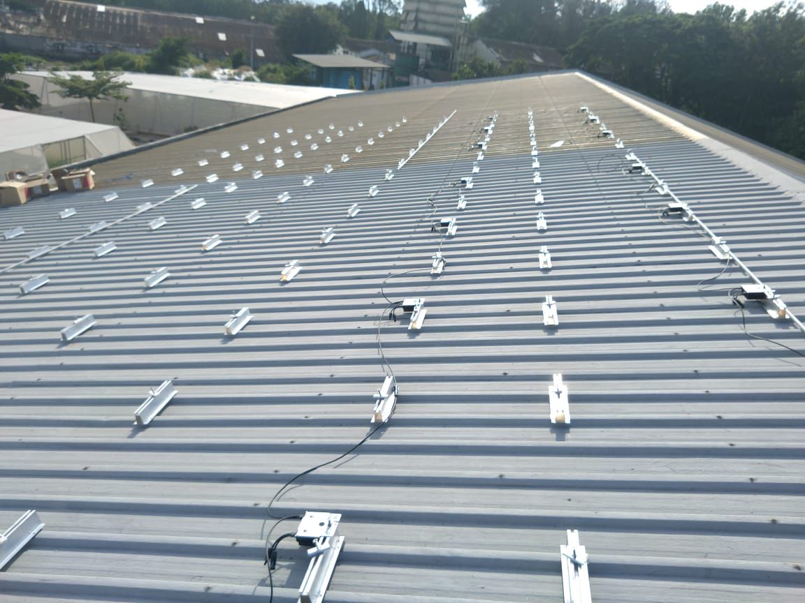 Aluminium mounting rails and clamps laid out across the metal sheet roof before module installation